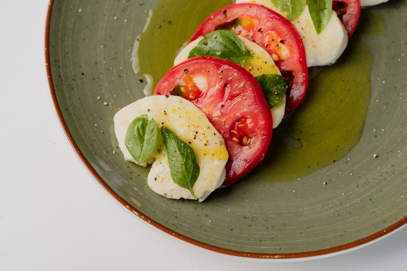 Ensalada caprese con mozzarella fresca hecha en casa, tomate y albahaca sobre un plato verde.
