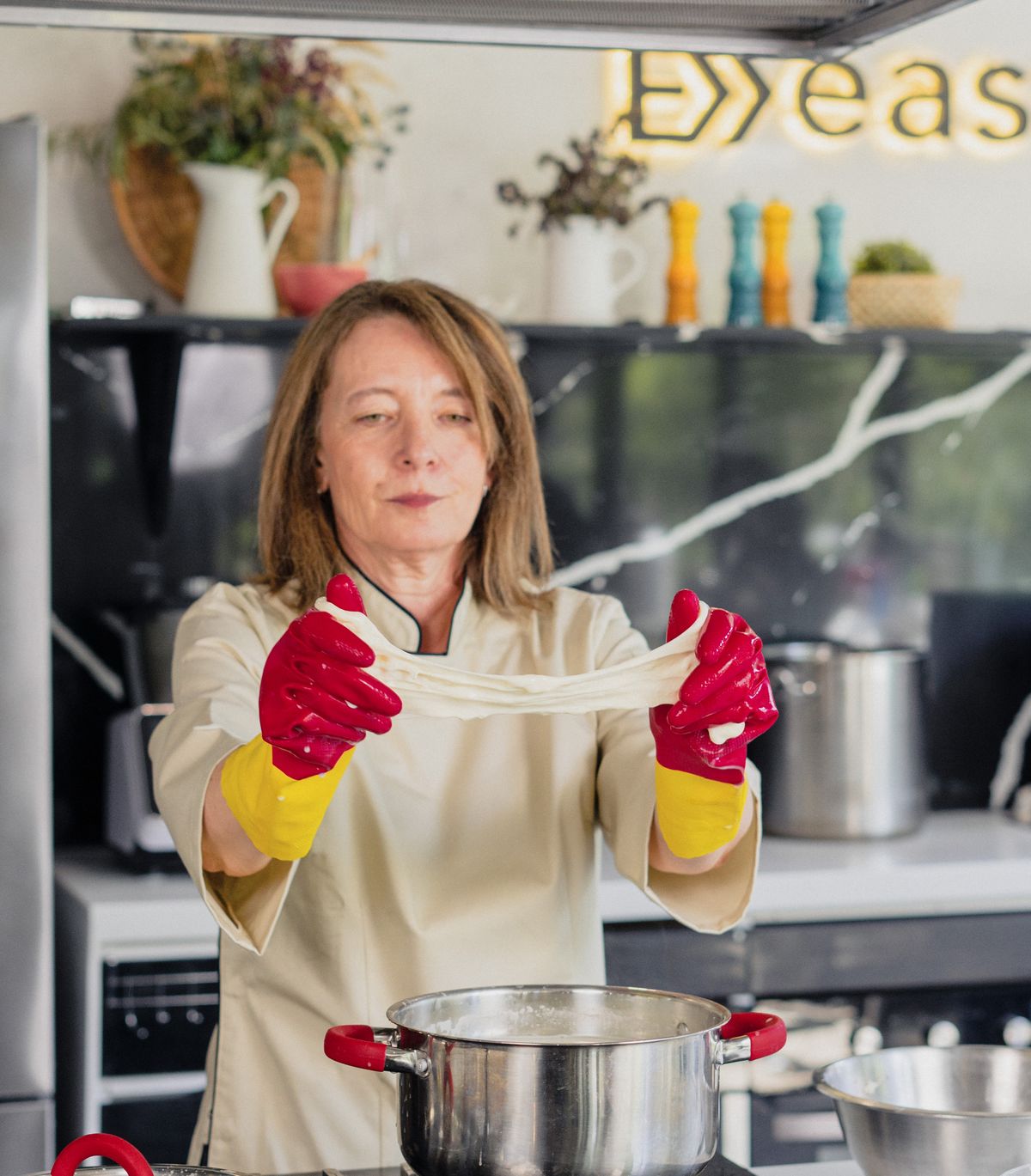 Las manos de Bernardita estirando la cuajada de mozzarella hasta formar un hilo continuo.