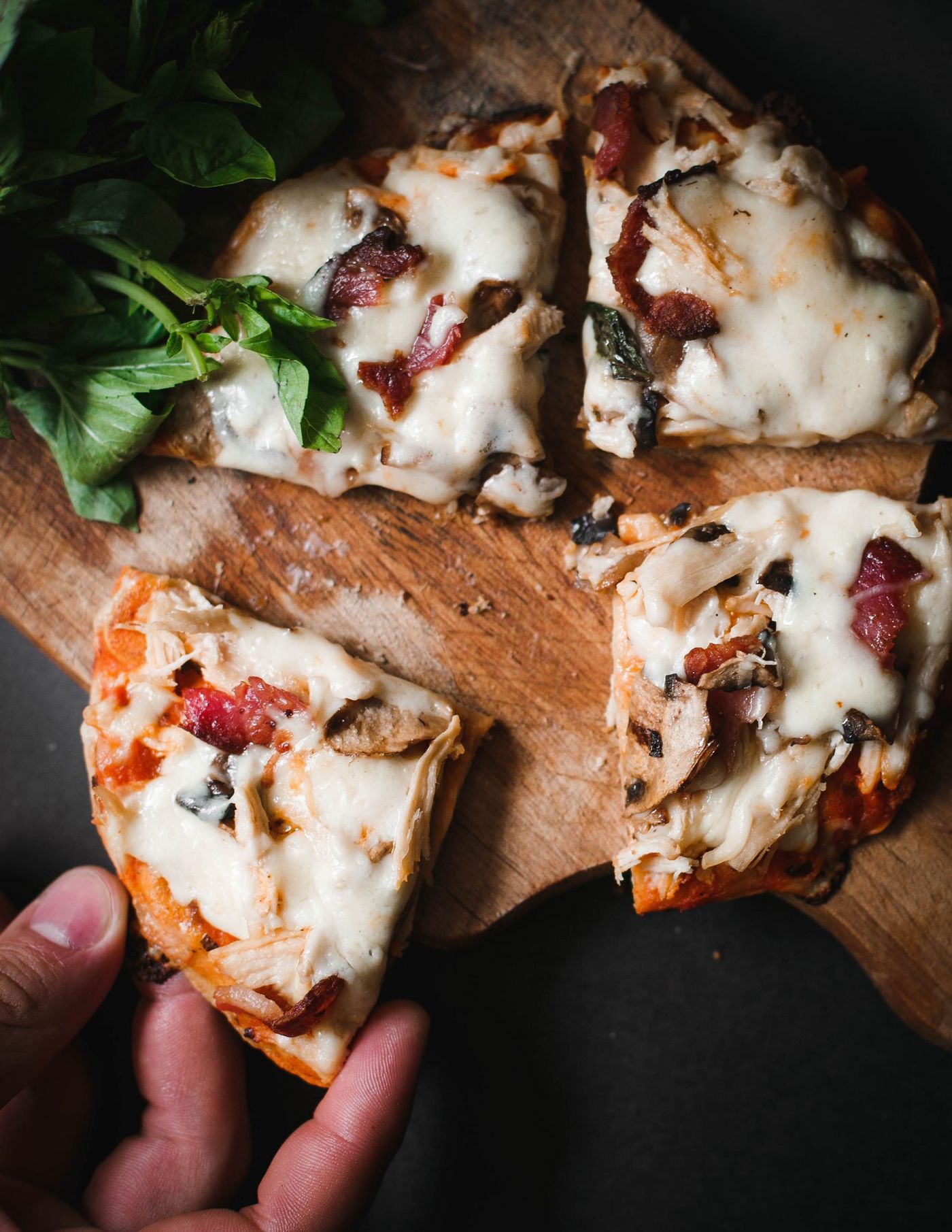 Pizza artesanal recién horneada con mozzarella fresca fundida y albahaca, cortada sobre una tabla de madera.